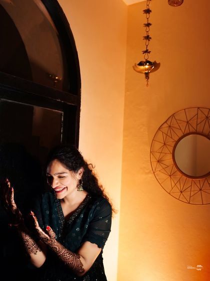 A candid shot of the bride laughing, her hands adorned with beautiful henna. This photo captures a moment of pure, unscripted happiness during her Mehendi.