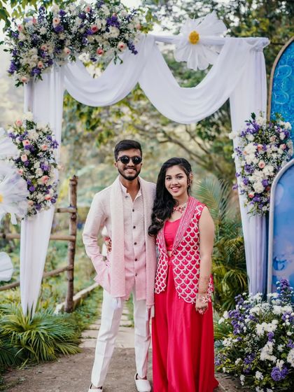 A happy portrait of the couple under a floral arch at their outdoor Haldi event.