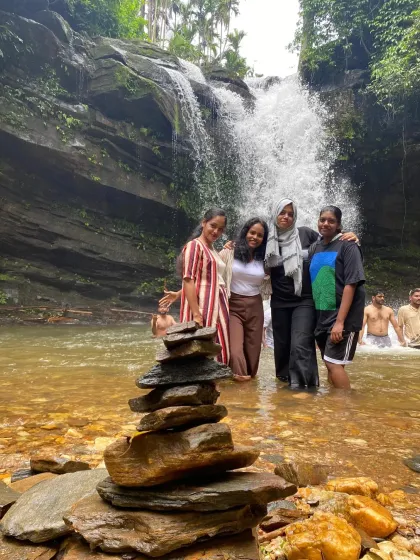 A group of friends posing for a photo in front of a waterfall, with a balanced rock stack in the foreground.
