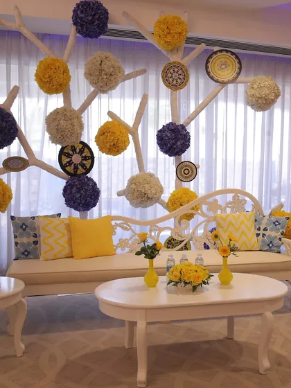 A modern and artistic seating area, with a white tree-like structure adorned with yellow and blue floral pom-poms and decorative plates.