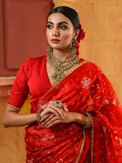 Another angle from the red saree shoot, this time with a more direct and powerful gaze. The lighting highlights the intricate jewelry and the model's confident expression.