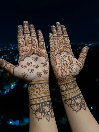 The palm-side view of Divya Spandana's mehendi, showing a mix of traditional butis and intricate floral work. One hand features a detailed peacock, while the other has scattered florals for a unique, asymmetrical style.