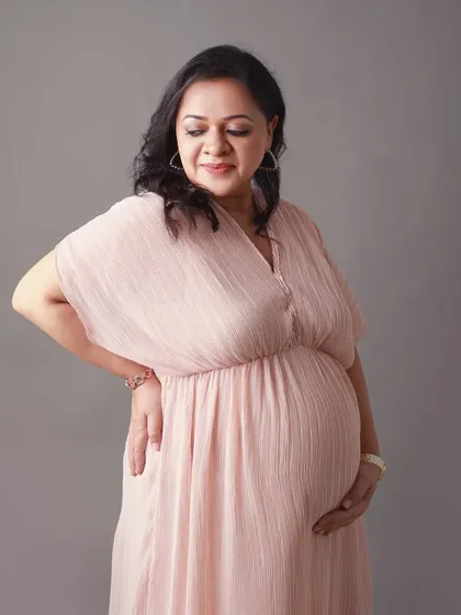 Dressed in a flowing pastel pink gown, this mother to be looks down at her bump with a soft smile. The grey studio background makes the colors pop beautifully.