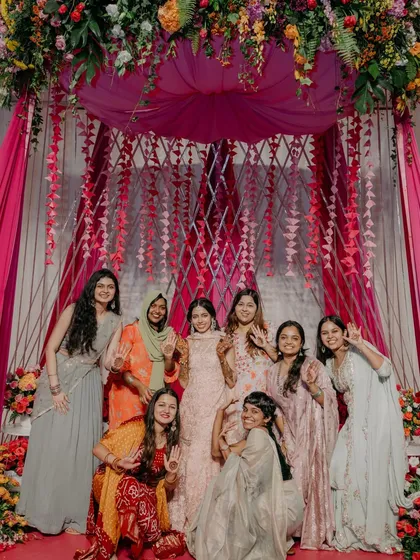 The bride and her friends posing for a photo in front of the beautiful pink Mehendi backdrop, capturing a moment of friendship and joy.
