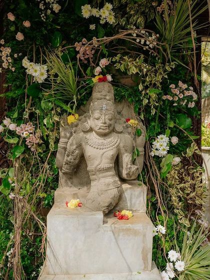 A stone statue at the entrance is adorned with a frame of fresh flowers and vines.