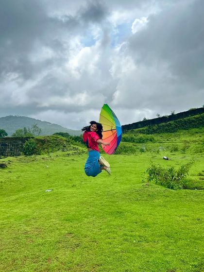 A joyful leap with a rainbow umbrella in the lush green fields near Kodachadri. The vibrant colors of nature and joy.