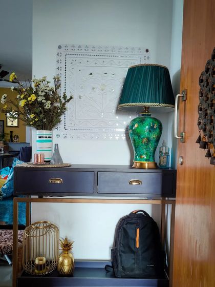 A stylish and functional entrance foyer. The emerald green lamp adds a bold splash of color, while the sleek console table provides a convenient spot for keys and mail. The Lippan art on the wall adds a touch of traditional craftsmanship.