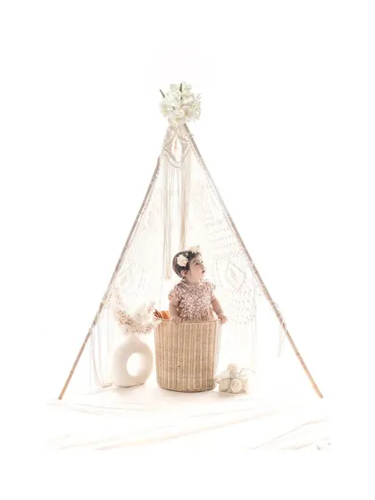 A wider view shows the baby in her basket, framed by a macrame teepee. This beautifully styled studio shot has a modern, bohemian feel, perfect for a unique first birthday session.