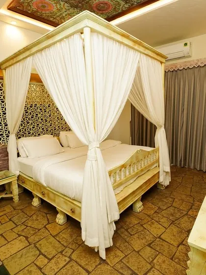 A wide-angle view of a vintage-themed luxury hotel room, centered on an elegant four-poster canopy bed with white drapes. This hospitality photography highlights the room's unique, ornate decor and spacious layout.
