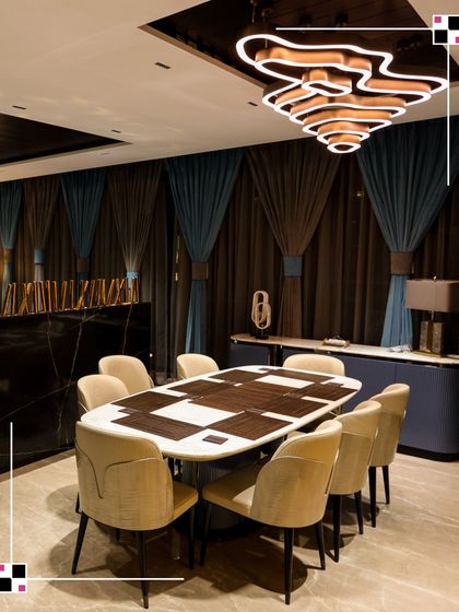 This dining room features a unique table with a wood inlay pattern, surrounded by plush velvet chairs. The dramatic curtains and modern wavy chandelier complete the look of moody sophistication.