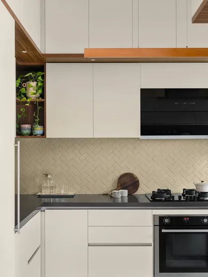 The kitchen in our 'Poorna' project is treated in subtle, muted tones. The herringbone-patterned tiles on the backsplash add a fresh dimension to the monochrome palette.