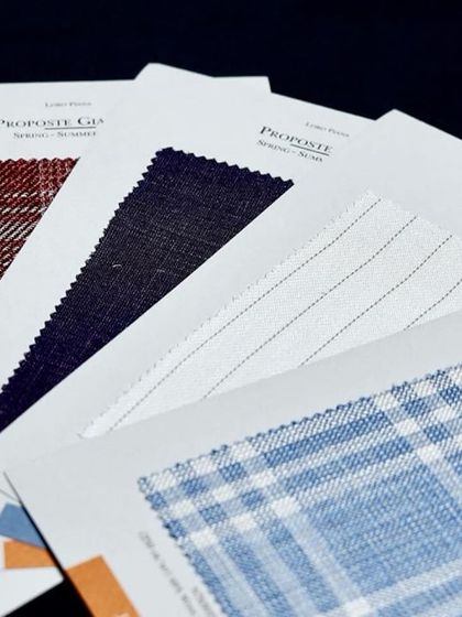 A selection of fabric samples laid out for a client. We help you choose from various patterns, including checks, pinstripes, and solids, for your gift.