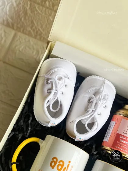 A close-up of the tiny white sneakers included in a pregnancy announcement box. Sometimes the smallest items make the biggest statement.