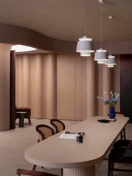 A long, minimalist table is set against a backdrop of undulating walls, showcasing how the space can transform to host meetings or events.