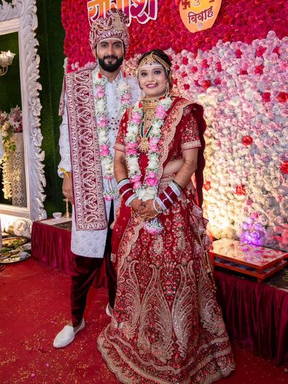 The happy couple posing against a wall of flowers. The bride's classic red wedding lehenga is the star of the show.