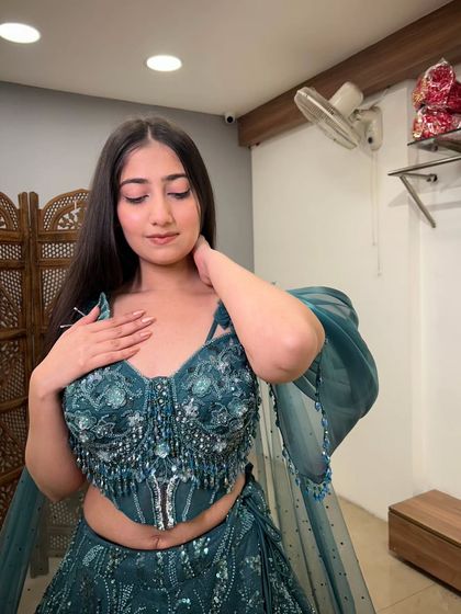 A close-up of the model in the teal gown, focusing on the intricate beadwork and sequin details on the corset-style blouse.