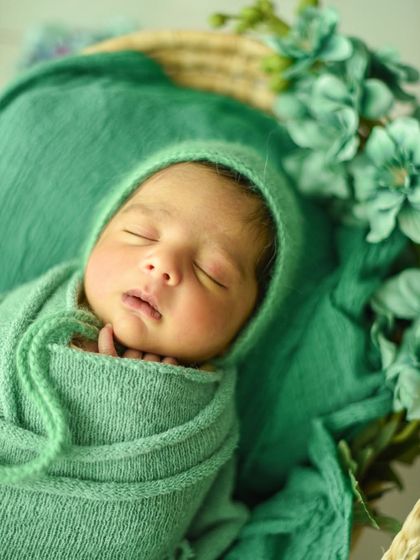 A detailed close-up of the baby's face, showing their delicate eyelashes and lips. The green bonnet frames their face perfectly.