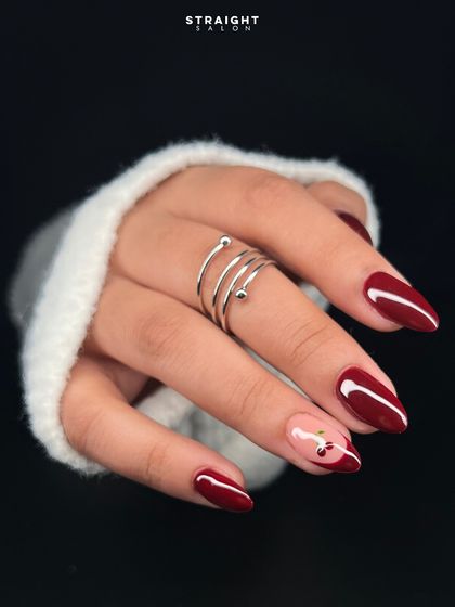 A classic deep red manicure with a playful twist. I hand-painted a delicate cherry design on a negative space accent nail for a touch of sweetness.