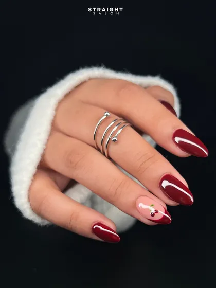 A classic deep red manicure with a playful twist. I hand-painted a delicate cherry design on a negative space accent nail for a touch of sweetness.