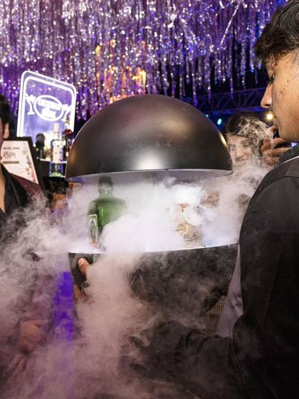 A drink is presented under a cloche filled with dramatic smoke. This serving style adds an element of mystery and surprise to our cocktail delivery.