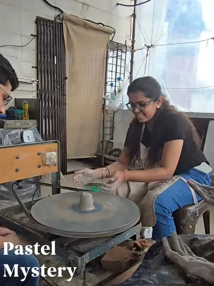 A snapshot of a couple's pottery session, with one partner smiling as she works on the wheel while her partner watches. The atmosphere is always relaxed and encouraging.