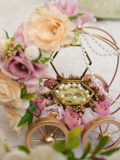 A close-up shot of the ring carriage, focusing on the intricate floral arrangement and the sparkling rings nestled inside the glass box.