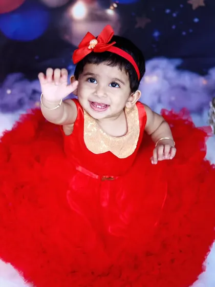A close-up of a baby girl in a red dress, waving during her magical, starry-sky themed shoot.