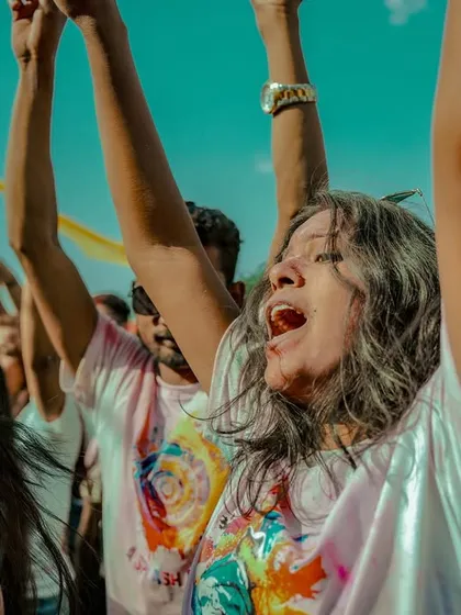 A partygoer completely immersed in the joy of the Holi celebration, singing along with her hands in the air.