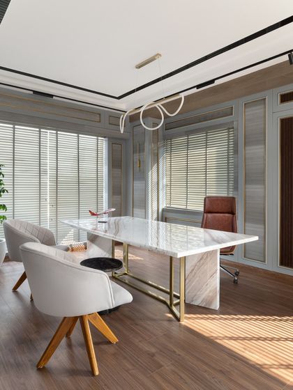 This angle showcases the elegant marble desk with its gold-finished base, paired with soft visitor chairs. The custom lighting fixture adds a sculptural element, completing the room's sophisticated aesthetic.