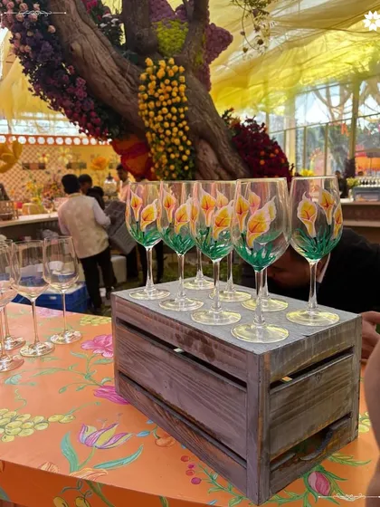 Hand painted wine glasses waiting for guests at a vibrant mehendi celebration. We believe that even the smallest details, like bespoke glassware, contribute to the overall experience.