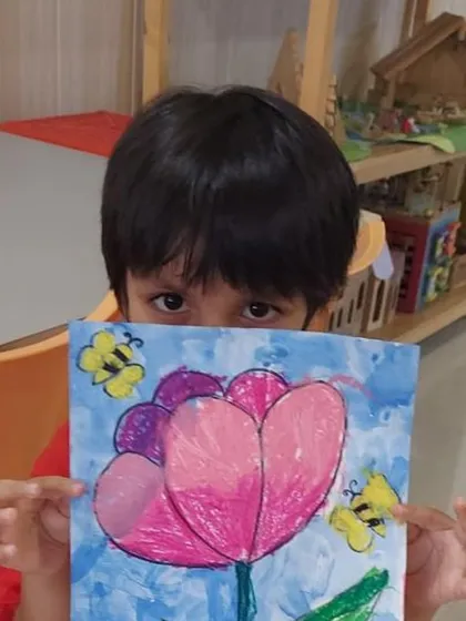 A shy artist peeking over his beautiful oil pastel drawing. We worked on blending techniques to create the soft petals of the tulip and the buzzing bees around it.