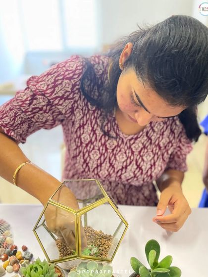 A participant carefully places the first layer of gravel in her geometric terrarium, the crucial foundation for proper drainage.