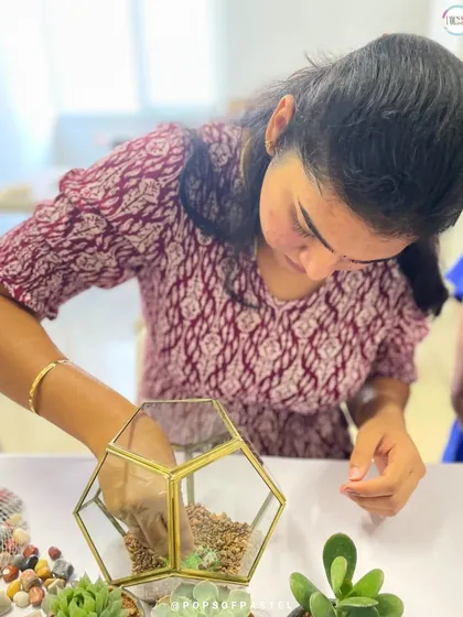 A participant carefully places the first layer of gravel in her geometric terrarium, the crucial foundation for proper drainage.