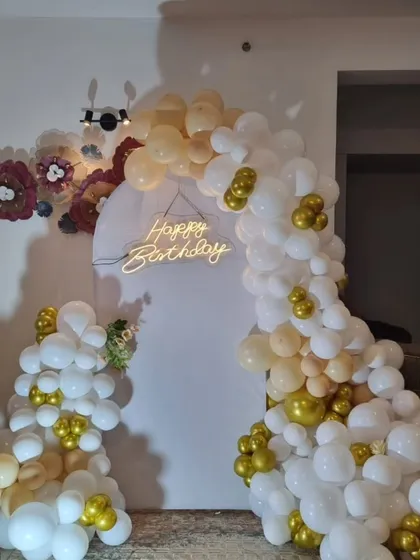 A modern and artistic birthday decoration with an organic white and gold balloon arch and paper flower accents.
