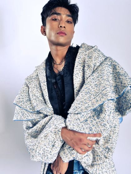 A portrait of a male model in a textured, oversized coat. The shot highlights modern menswear with an artistic flair.