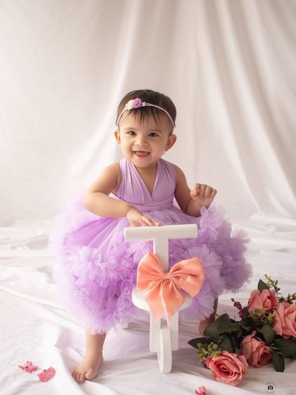 The biggest smile for her first birthday! Posing with a little white tricycle, she is the picture of pure joy.