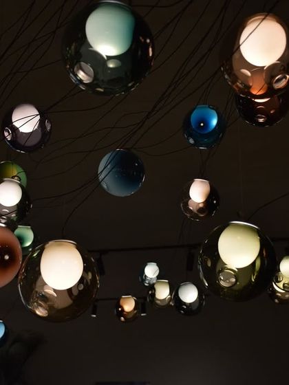A constellation of Bocci 28 series pendants in various colors and sizes creates a mesmerizing effect in a dark room. This image captures the magic of the series, where each sphere contains its own miniature world of light and shadow.