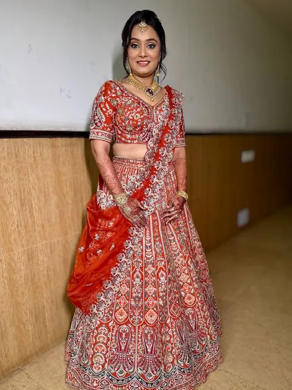 A stunning look for a child's Mundan Ceremony. The client is wrapped in the warmth of a marigold-orange lehenga, and her makeup is glamorous and elegant.