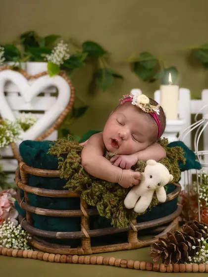 This cozy, rustic setup features a baby sleeping in a wooden sleigh, surrounded by pinecones, greenery, and a warm, mossy blanket.