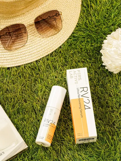 A summer-themed flatlay featuring the product on a bed of grass with a sunhat and sunglasses. This composition evokes a feeling of a sunny day out, positioning the skincare as a perfect companion for outdoor activities.