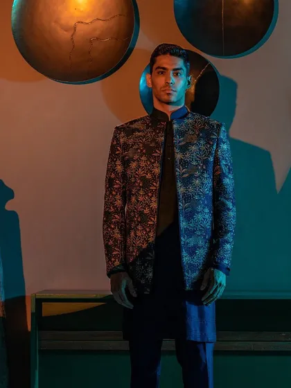 A model stands poised in a dark, intricately embroidered jacket, a key piece from our Raaya collection. This Indo-Western ensemble is designed for the man who appreciates a blend of traditional craft and modern form.
