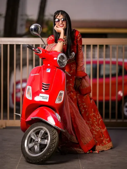 The full look of the modern Vespa bride, showing off her red lehenga and cool sunglasses against an urban backdrop.