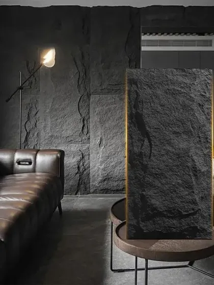 A moody and sophisticated living room with walls covered in our black PU stone panels, creating a perfect backdrop for a modern leather sofa.