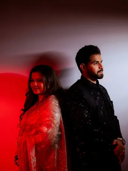 A creative couple portrait from a wedding event. The bride and groom stand back-to-back against a red and white lit wall, creating a chic and dramatic image.