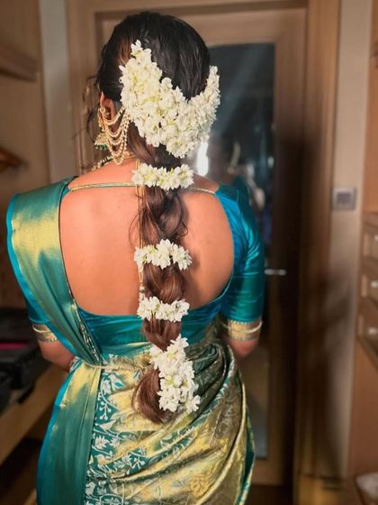 A beautiful South Indian bridal braid adorned with sections of fresh jasmine flowers. This style, known as a "poola jada," is a fragrant and visually stunning choice for a traditional wedding.