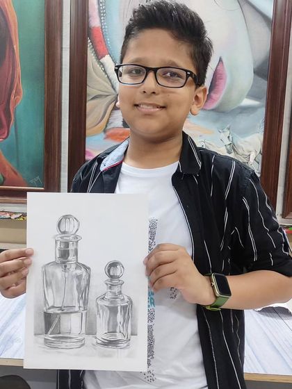 A young student proudly displays his still life drawing of glass bottles, demonstrating excellent control over shading and capturing reflections with a pencil.