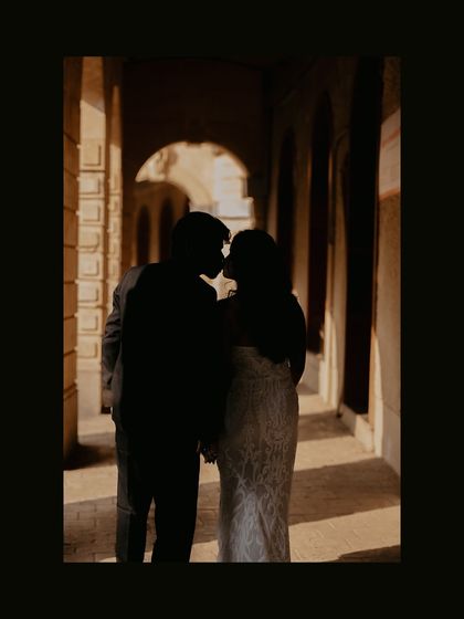 A beautiful silhouette of the couple sharing a kiss in a sunlit stone corridor, creating a dramatic and romantic image.