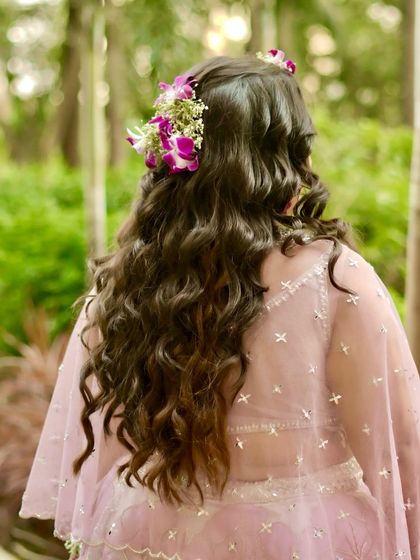 A back view of a gorgeous hairstyle for a Haldi ceremony. The long, loose curls are decorated with fresh orchids, tying the whole look together.