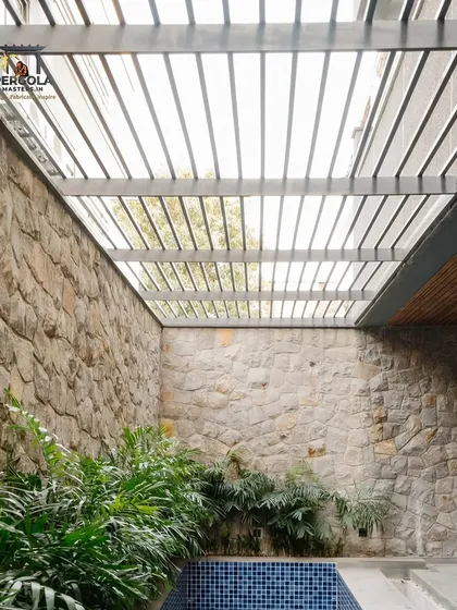 This rafter pergola is built within a courtyard, framed by stone walls and overlooking a small pool. The design creates a private, tranquil retreat that feels both rustic and modern.