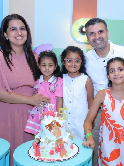 A family celebrates their daughter's 5th birthday with a beautifully decorated cake.